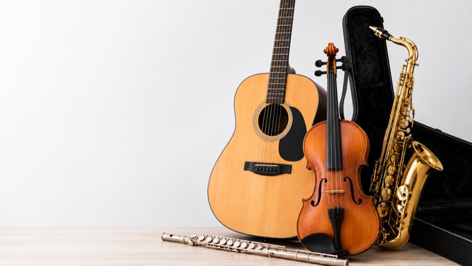 Violão, violino, saxofone e flauta apoiados sobre bancada de madeira, ao lado de estojo preto